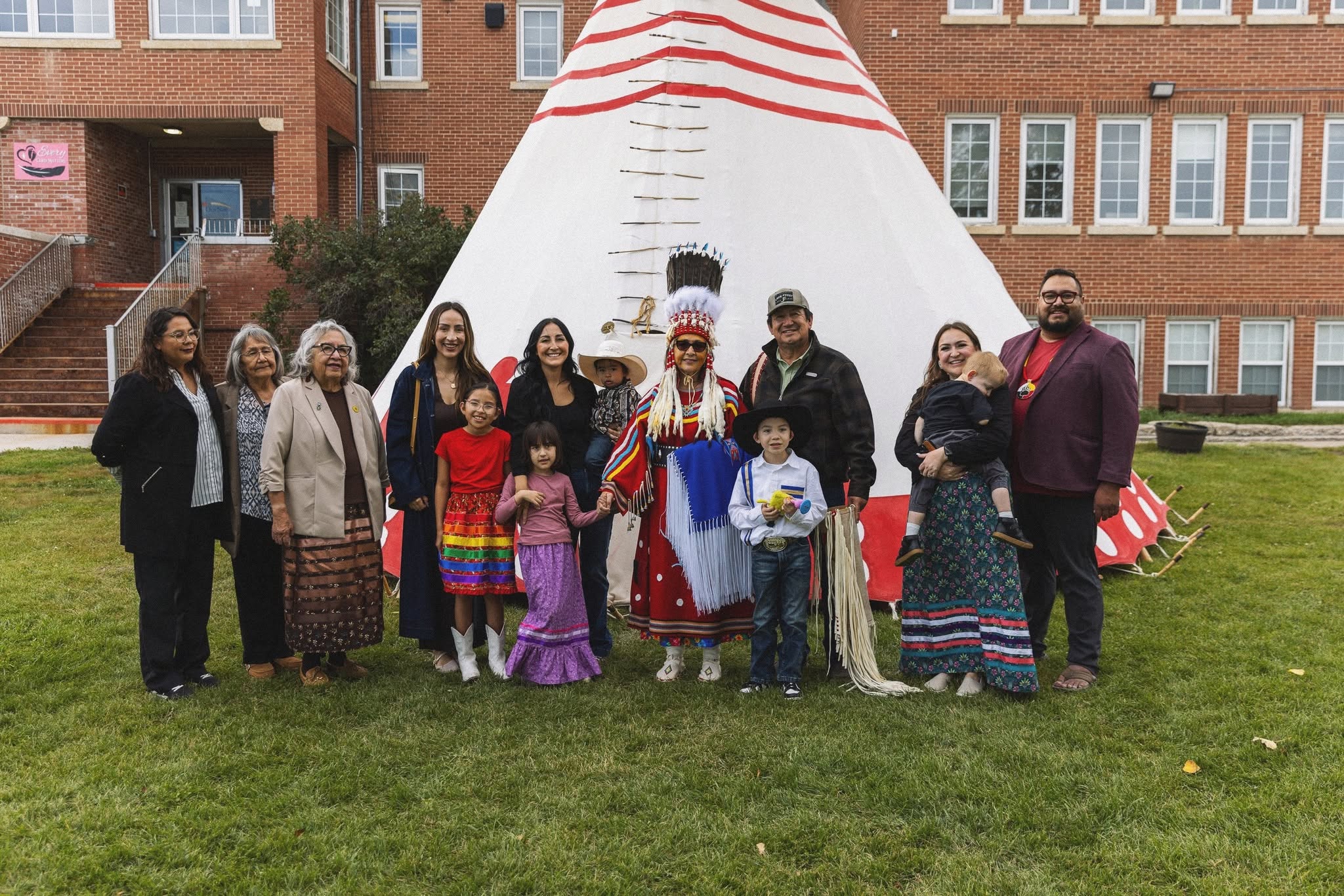 A group of family, Elders and community members posing together in front of the tipi