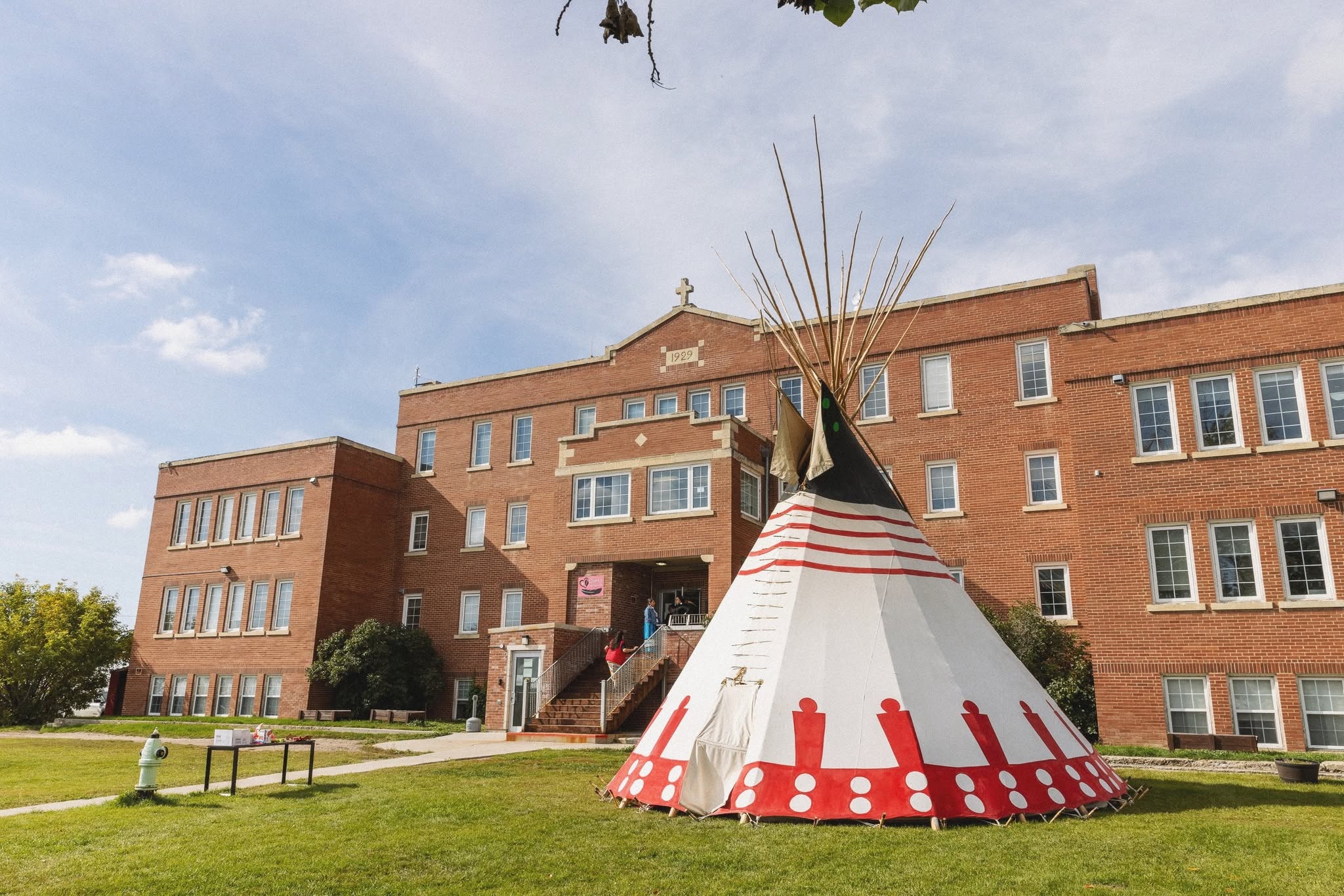 A painted tipi on the lawn in front of the 1929 brick Old Sun Community College building